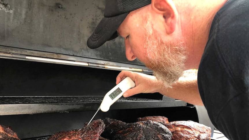 A man uses an electronic temperature gauge to check heat of meat on barbecue