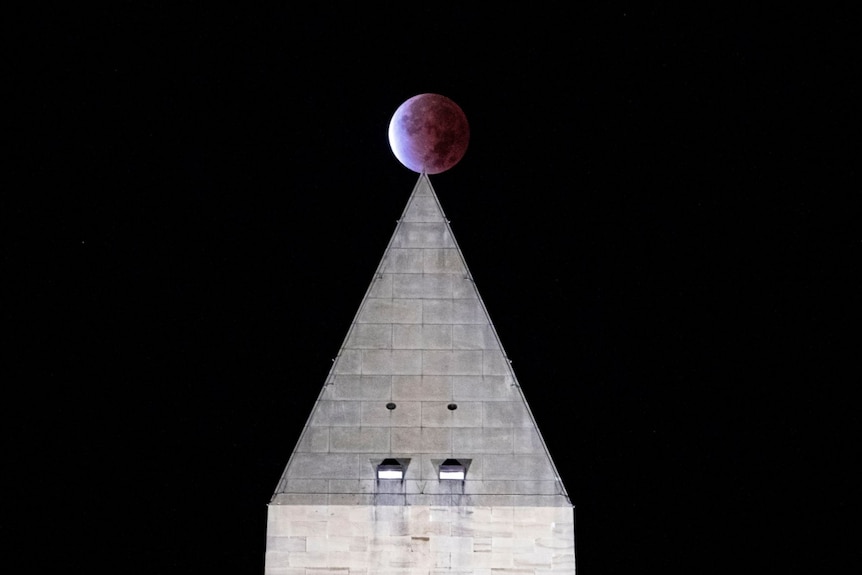 A partially eclipsed moon creatively photographed above the point of a triangular roof at night
