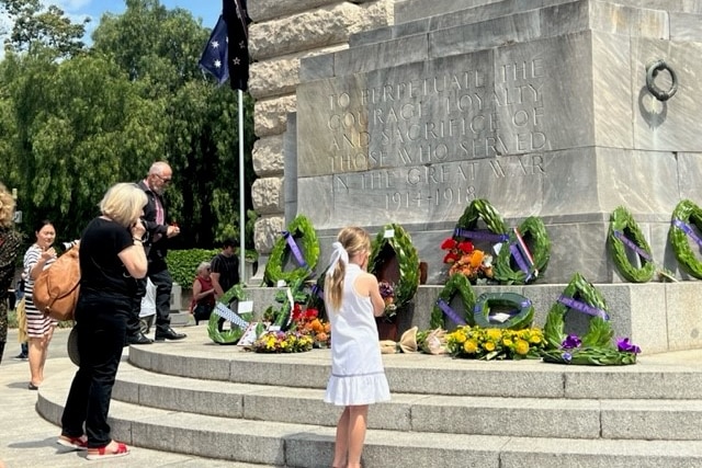 Two people look up at a war memorial that has wreathes laid at the base.