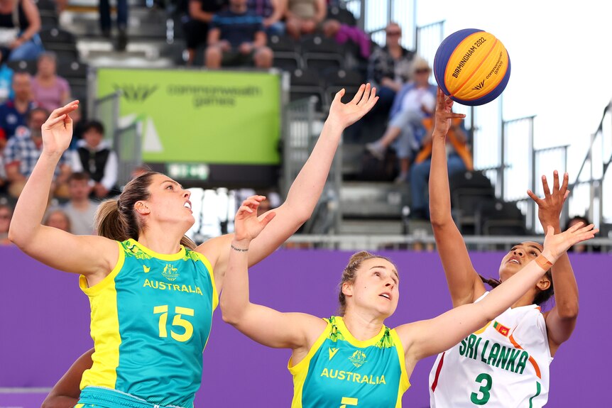 Two Australian women's 3x3 basketballers jump for the ball along with a Sri Lankan opponent.