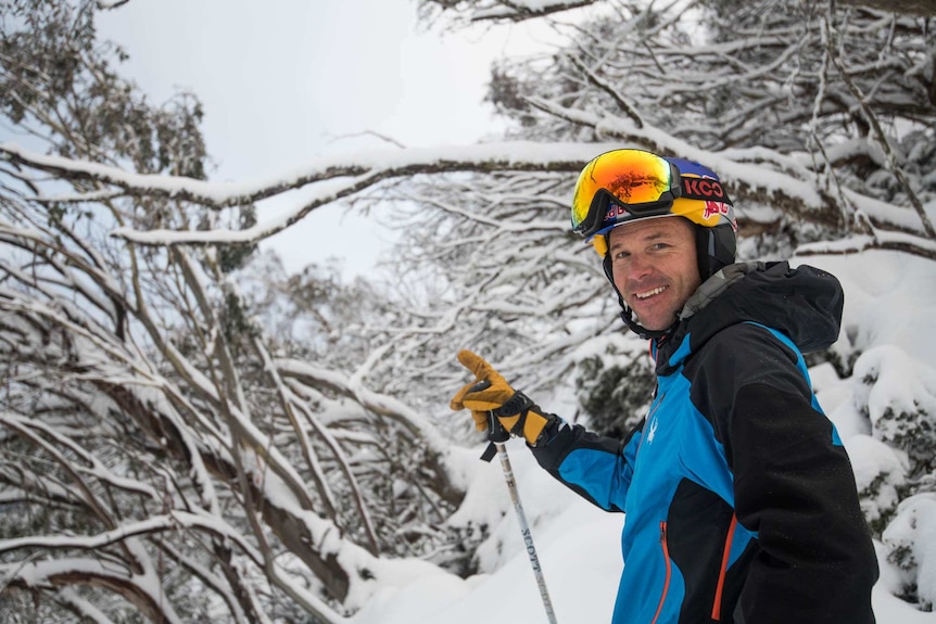 A man stands in ski gear in front of a snowy landscape.