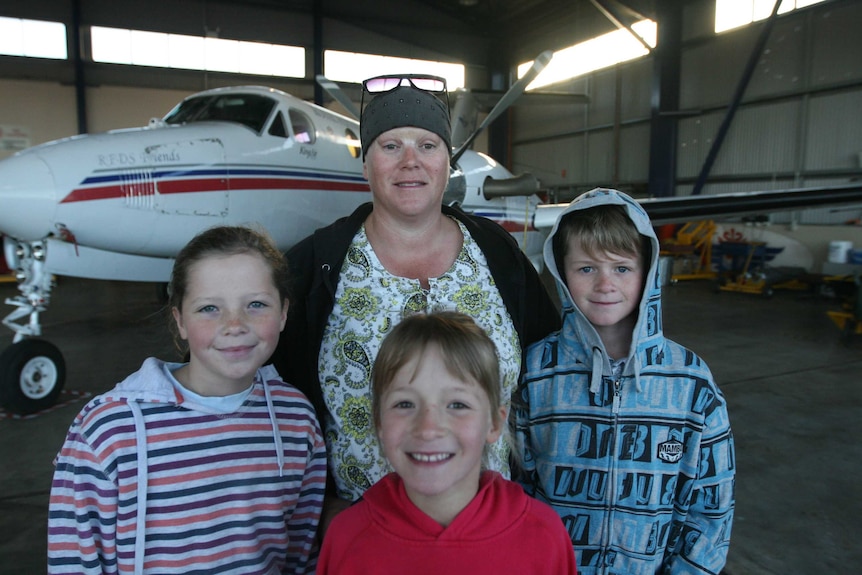 Woman and three children stand in hangar with aircraft
