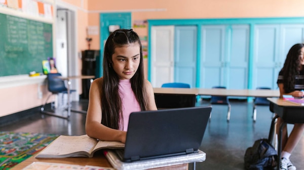 Student in classroom sitting at desk in front of her laptop.