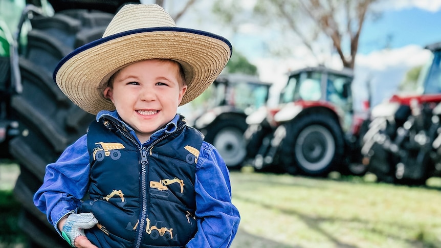 a close up image of a young boy standing in front of tractors