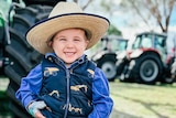 a close up image of a young boy standing in front of tractors