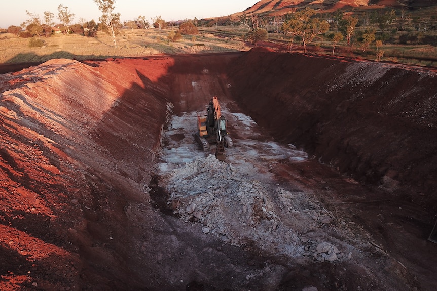 Image of a digger in a pit containing scraps and rubble at Wittenoom, Western Australia.
