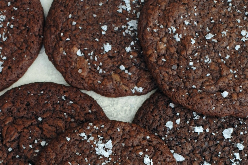 A pile of chocolate brownie cookies sprinkled with sea salt, the base for ice cream sandwiches.