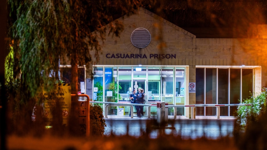 The front entrance of Casuarina Prison at night as people mill around outside
