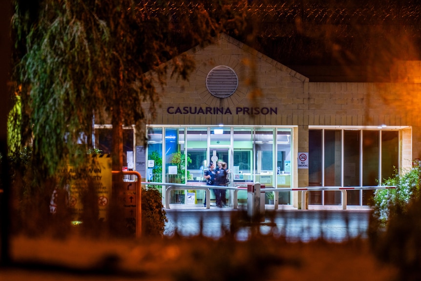 The front entrance of Casuarina Prison at night as people mill around outside