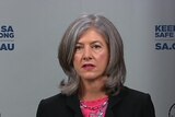 A woman with grey hair wearing a black blazer and a pink shirt