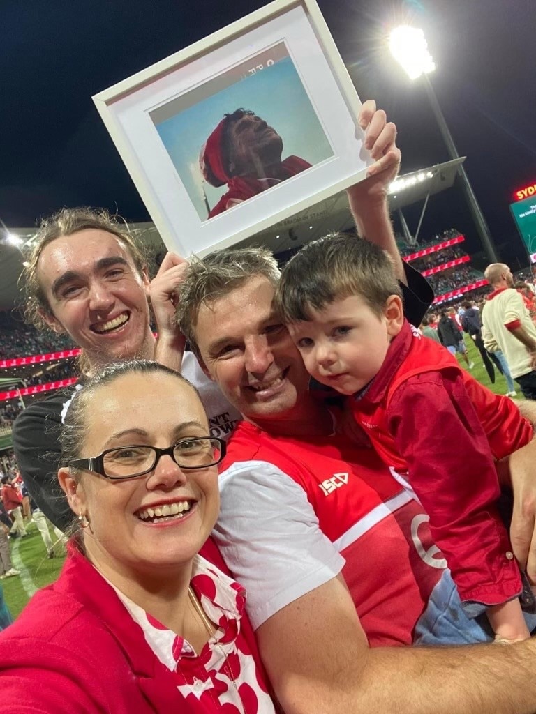 A group of people smile at the camera while holding a picture of an old lady in the air