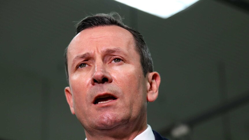 Mark McGowan wearing a red tie in front of a microphone