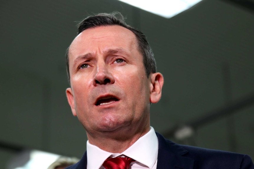 Mark McGowan wearing a red tie in front of a microphone