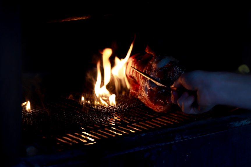 a roast duck is held by large tweasers over a flame grill