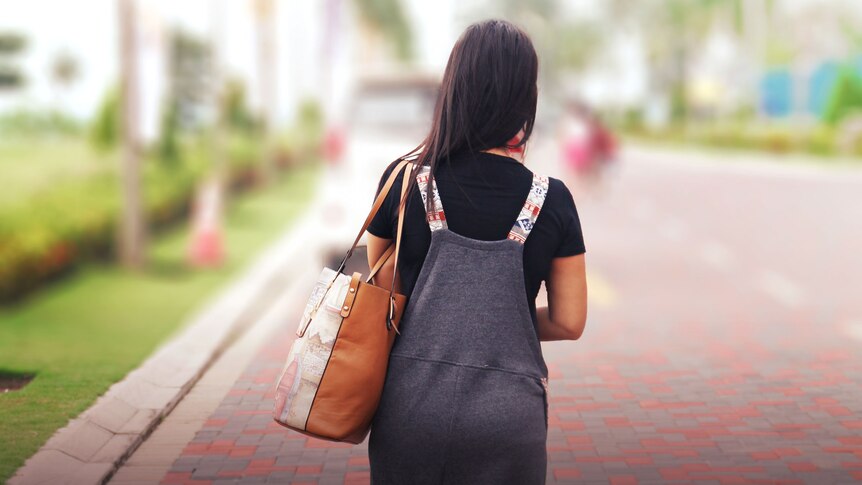 A woman carrying a handbag walks away from the camera down a street