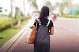 A woman carrying a handbag walks away from the camera down a street
