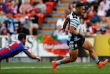 An NRL player stretches out to elude a tackle as he runs away from a defender.