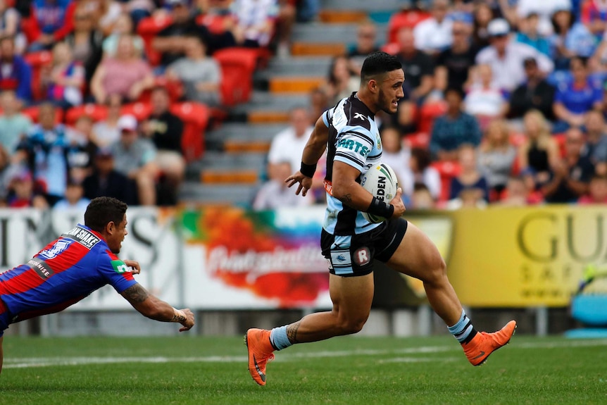 An NRL player stretches out to elude a tackle as he runs away from a defender.