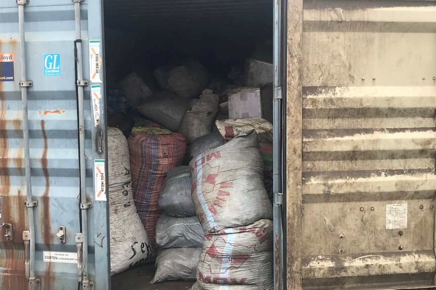 A shipping container with its doors ajar, revealing many sacks full of contents
