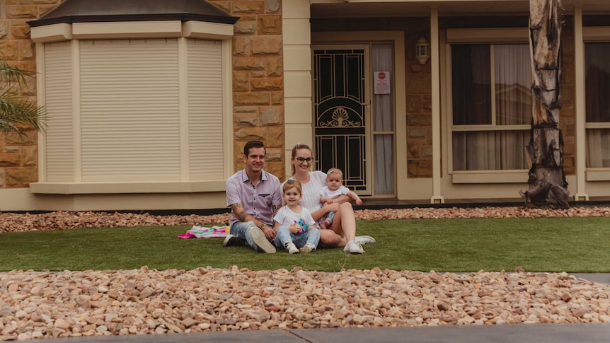Lachlan and Richelle McOmish sit on turf with their daughters Penny, 4, and 5-month-old Scarlett.