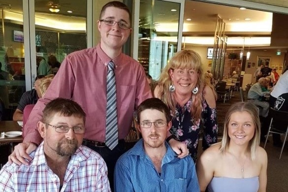 Family of five grouped at restaurant table, son and mother standing with father, son and daughter sitting 