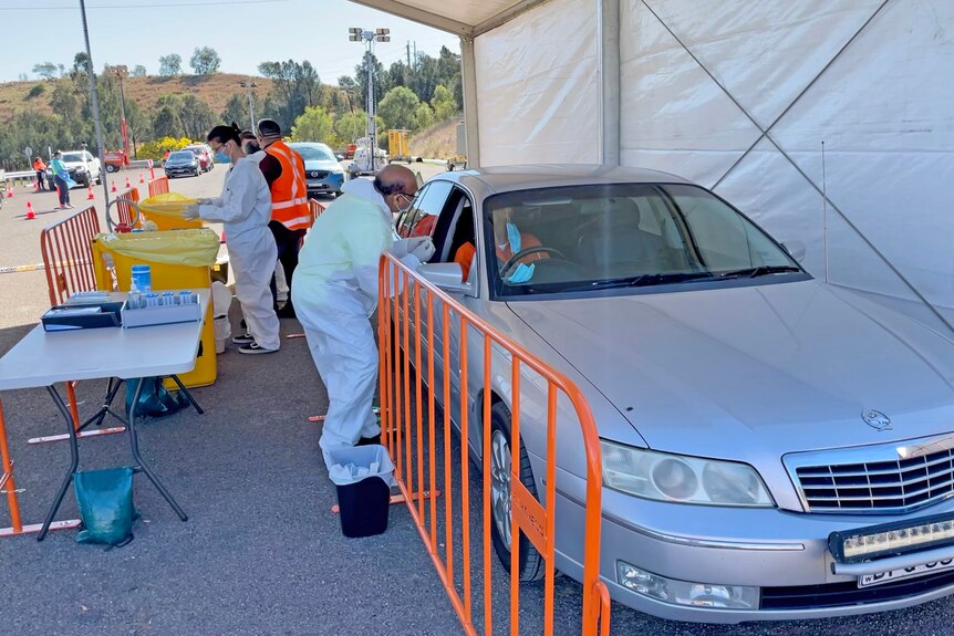 Health workers in PPE administer tests to people in their cars