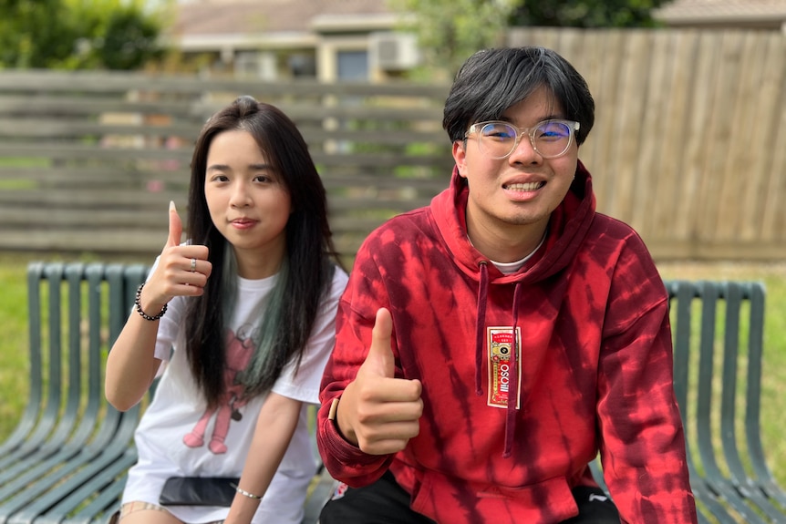 Sally Liu and Lee Li smile and sit together on a park bench.