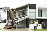 people walking along a footpath looking at a house that has collapsed