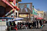People walk through a security checkpoint into the Hotan Bazaar where a screen shows Chinese President Xi Jinping.
