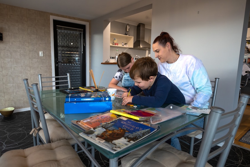 A mum at a table watches over her two children painting