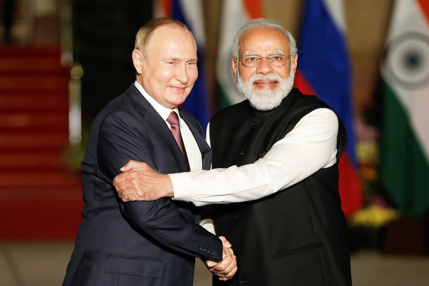 Vladimir Putin grinning while shaking hands with Narendra Modi