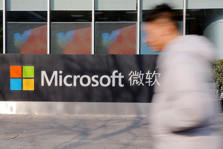 A man moves quickly past the outside of a building where a corporate logo is prominently displayed.