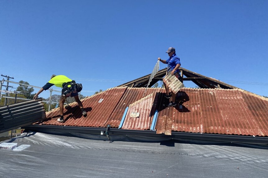 Two men on a roof taking off old iron roof sheets.