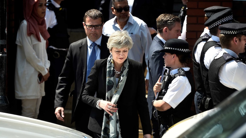 Theresa May walks out of a mosque surrounded by police and other people.