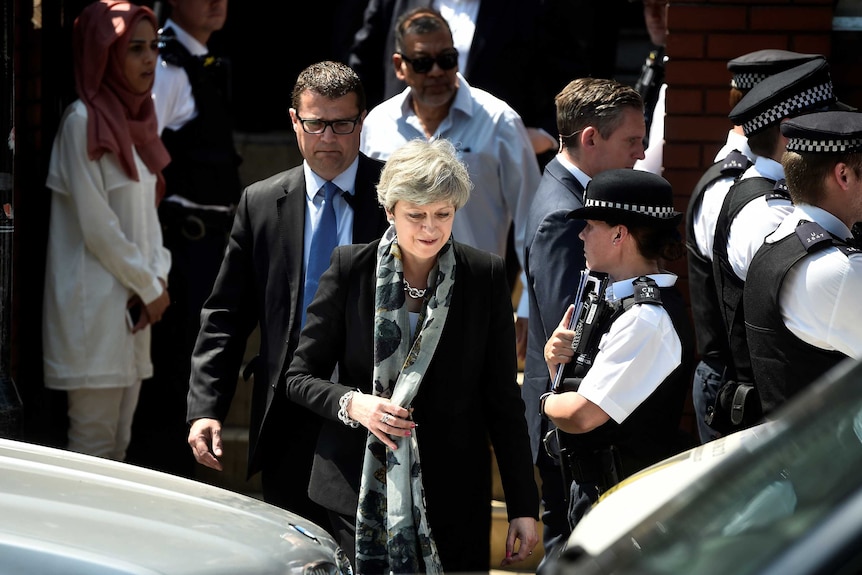 Theresa May walks out of a mosque surrounded by police and other people.
