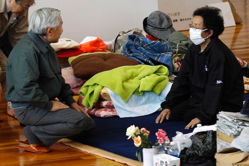 Akihito kneels down to speak to a woman at a Fukushima evacuation centre in 2011