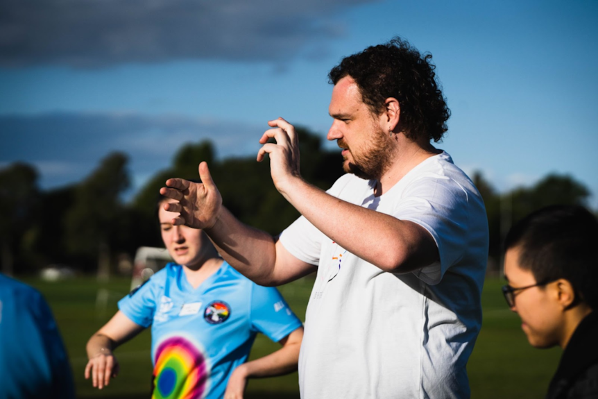 A man wearing a white shirt has his arms raised as he gives instructions to players.