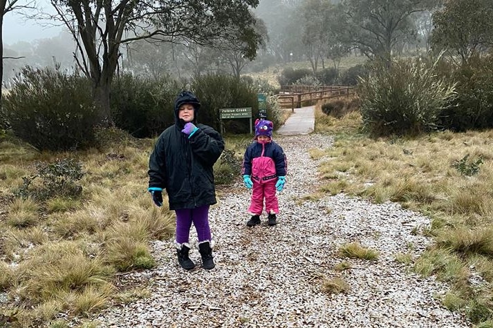 Two children in snow jackets stand on a walking track covered in snow.