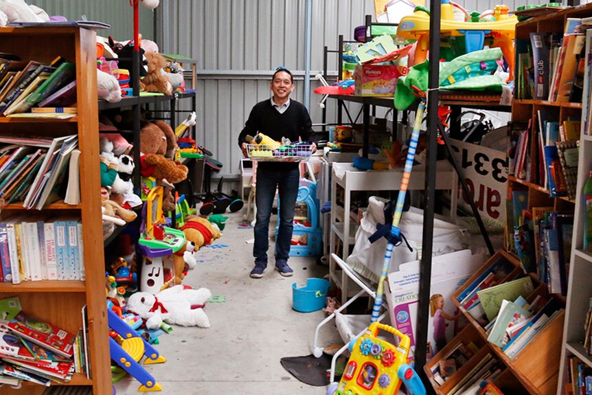 Man holding a basket full of old toys in an aisle filled with colourful books and old toys.