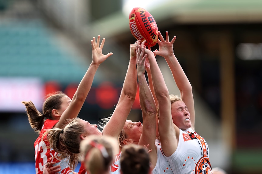 Sydney and GWS players raise their hands towards the football in a contest