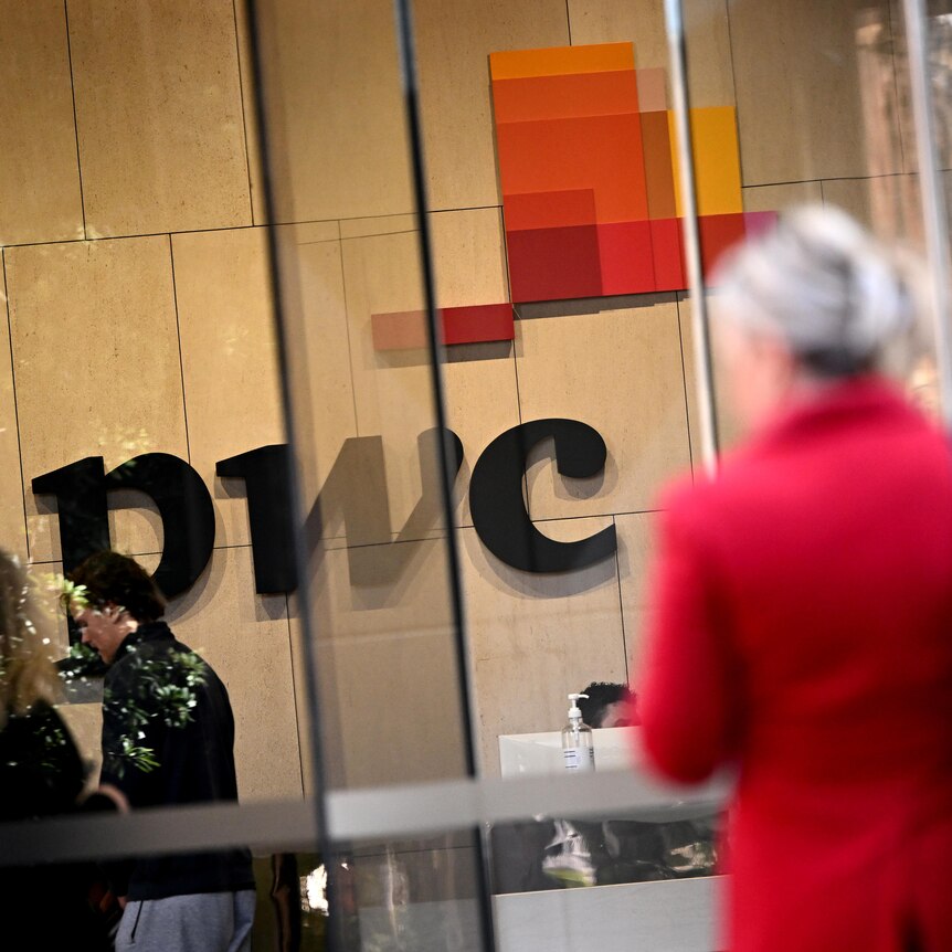 The PWC sign inside its lobby, with a woman in a red jacket walking by