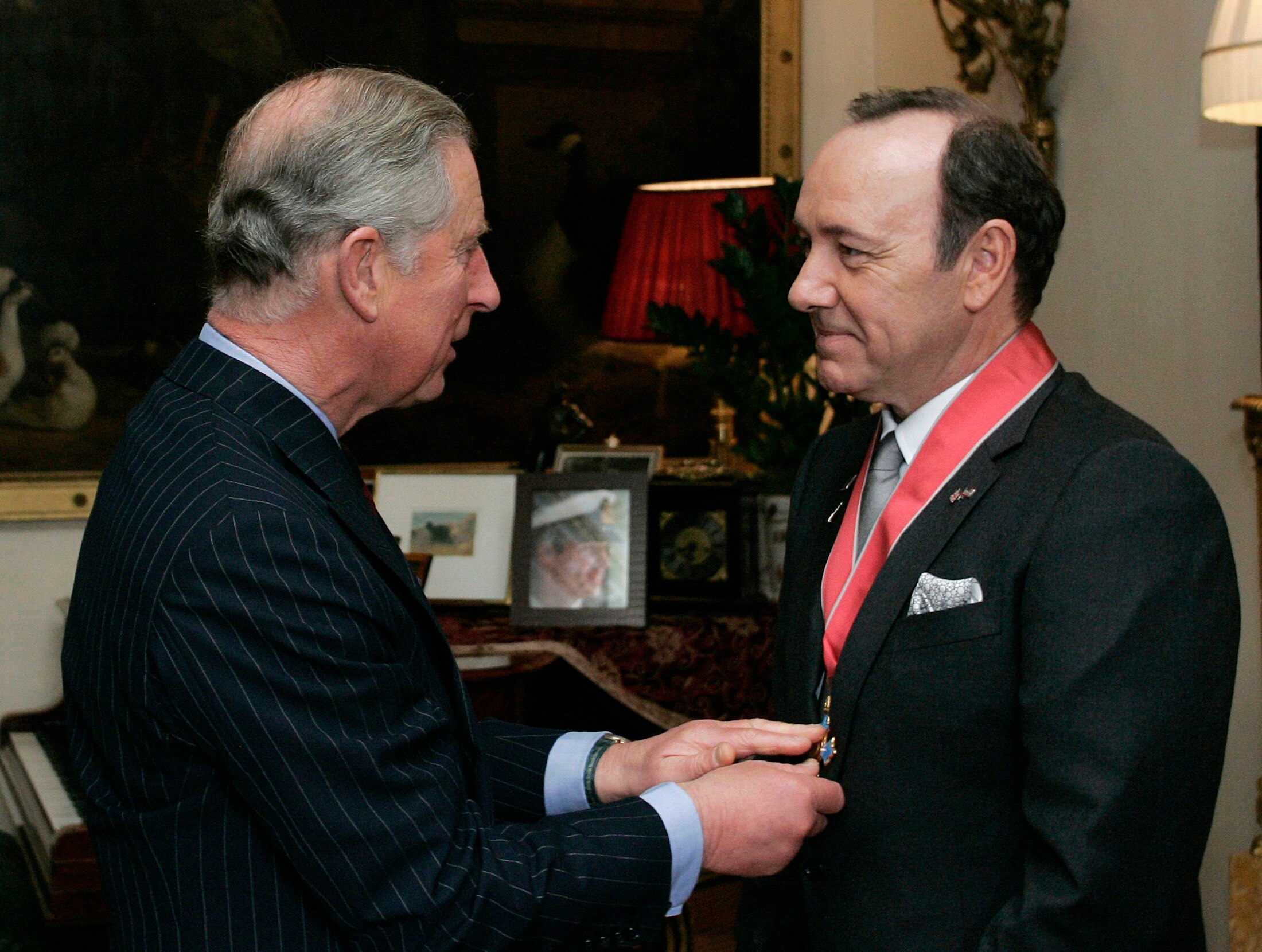 King Charles putting a red ribbon around Kevin Spacey's neck