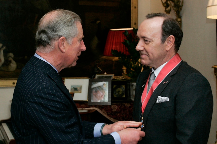 King Charles putting a red ribbon around Kevin Spacey's neck