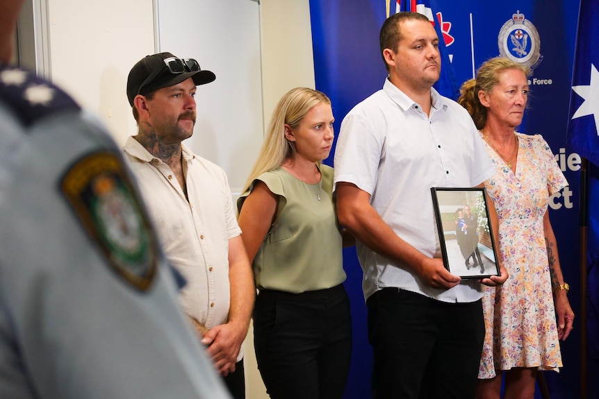 A family stand with a photo at a press conference alongside police