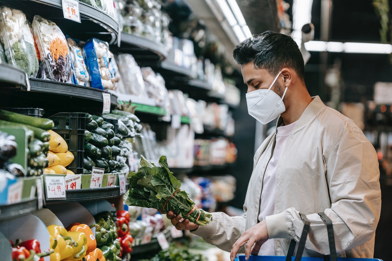 A young man carrying a basket grabs a bunch of spinach in a supermarket.