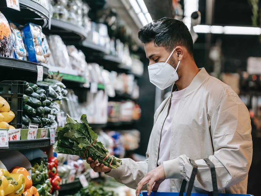 A young man carrying a basket grabs a bunch of spinach in a supermarket.