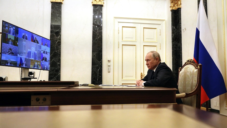 Russian President Vladimir Putin sitting at a table on a video conference call with members of his security council.