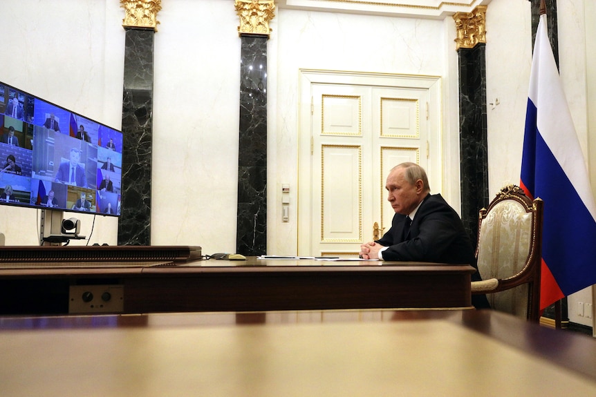 俄罗斯总统弗拉基米尔·普京坐在一张桌子旁，与他的安理会成员通电话。