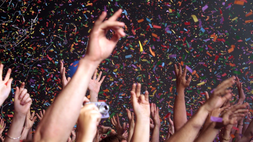 Photo of a crowd with hands raised at a music festival, with confetti falling around them