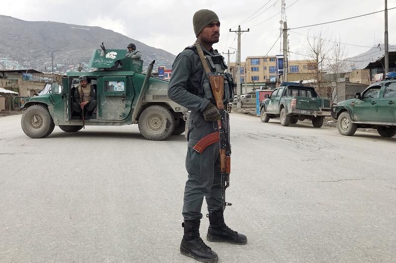 An Afghan policeman with a gun and police truck in the background.